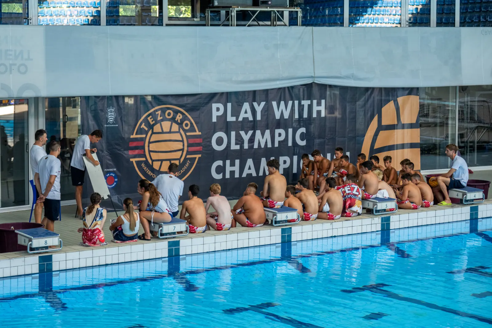 Campers lined up on the pool deck under the Play With Olympic Champions banner